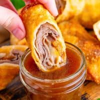 A hand dipping a piece of a French Dip Egg Roll in sauce.