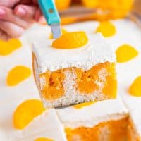 A piece of Orange Creamsicle Poke cake being held over the baking dish with the rest of the cake.
