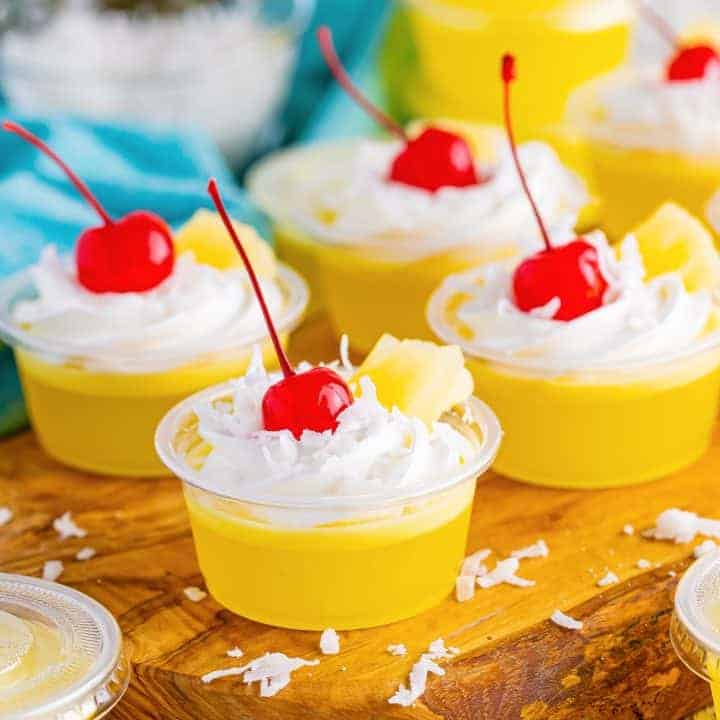 Close up looking at 4 Pina Colada Jello Shots with whipped cream, cherries, and pineapple bits.
