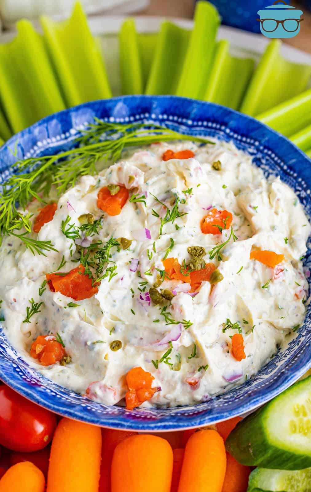 A blue serving bowl with smoked salmon dip and some vegetables around it for dipping.