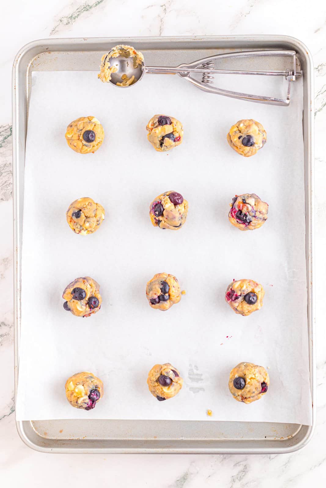 Balls of blueberry cookie dough on a parchment lined baking sheet.