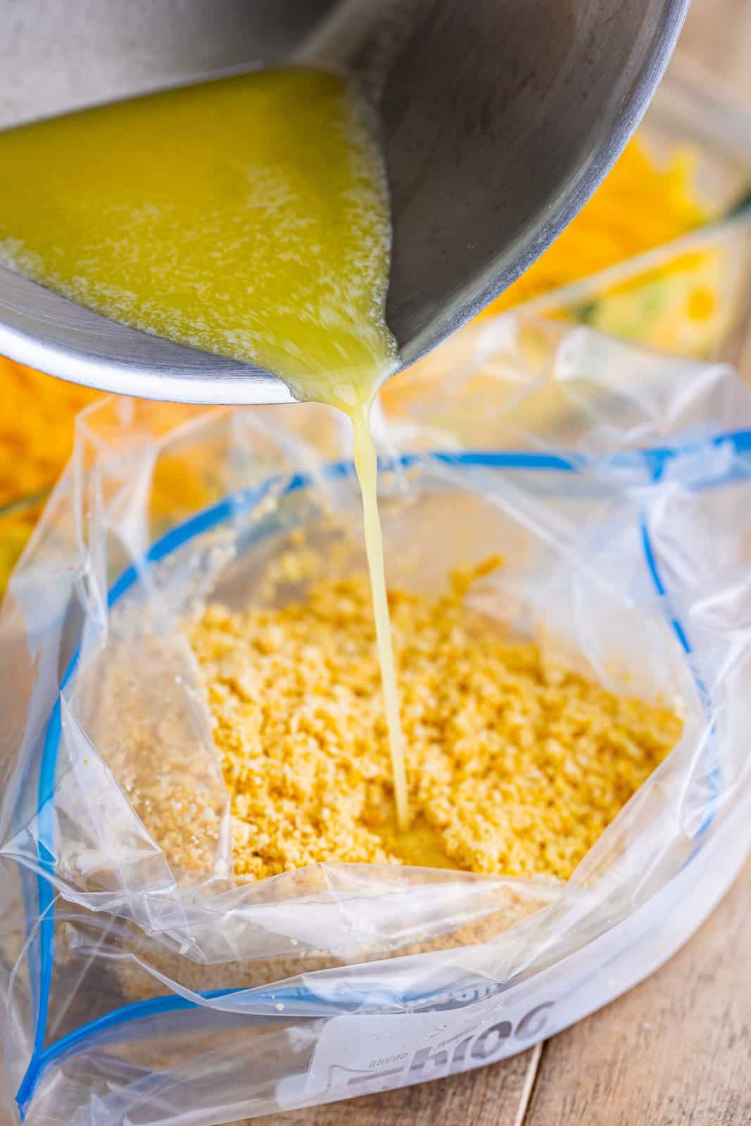 Some melted butter being poured into a bag of crushed crackers.
