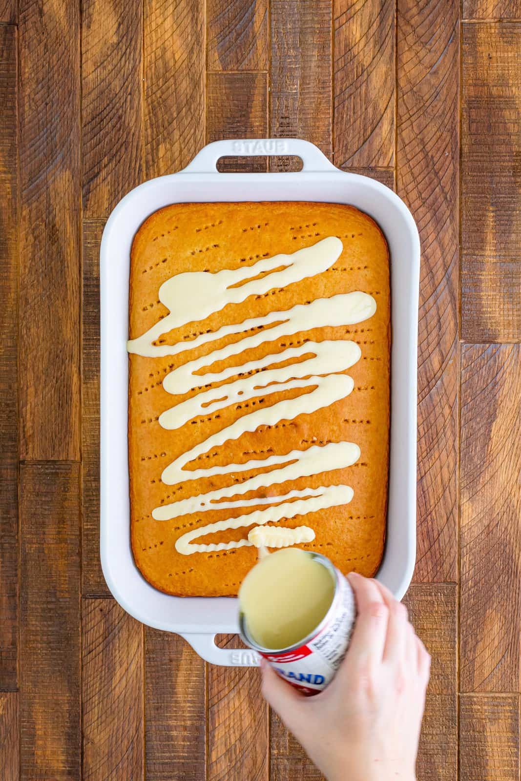 Sweetened condensed milk being poured all over a fresh baked cake.