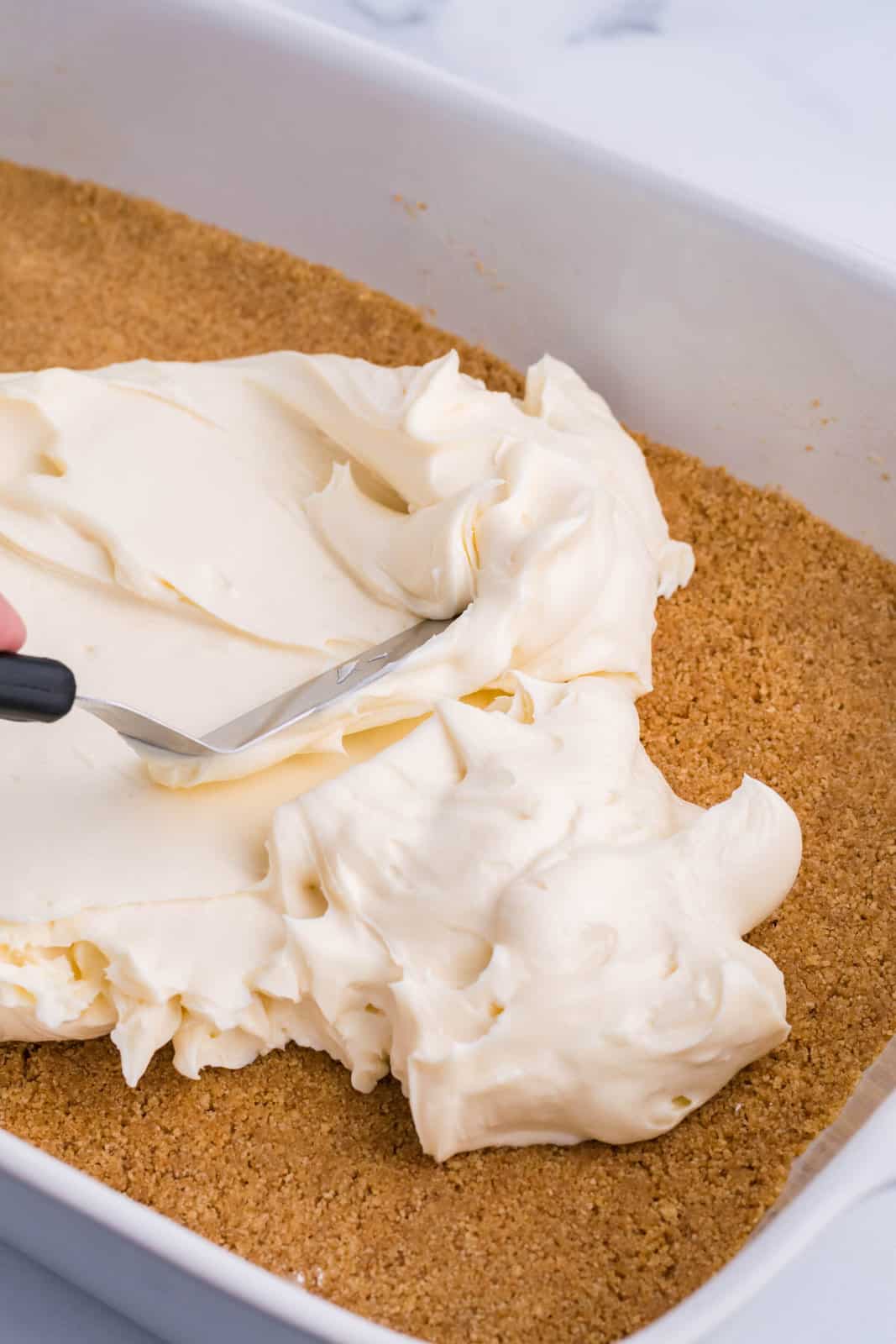 Cream cheese layered being spread out on a graham cracker crust. 