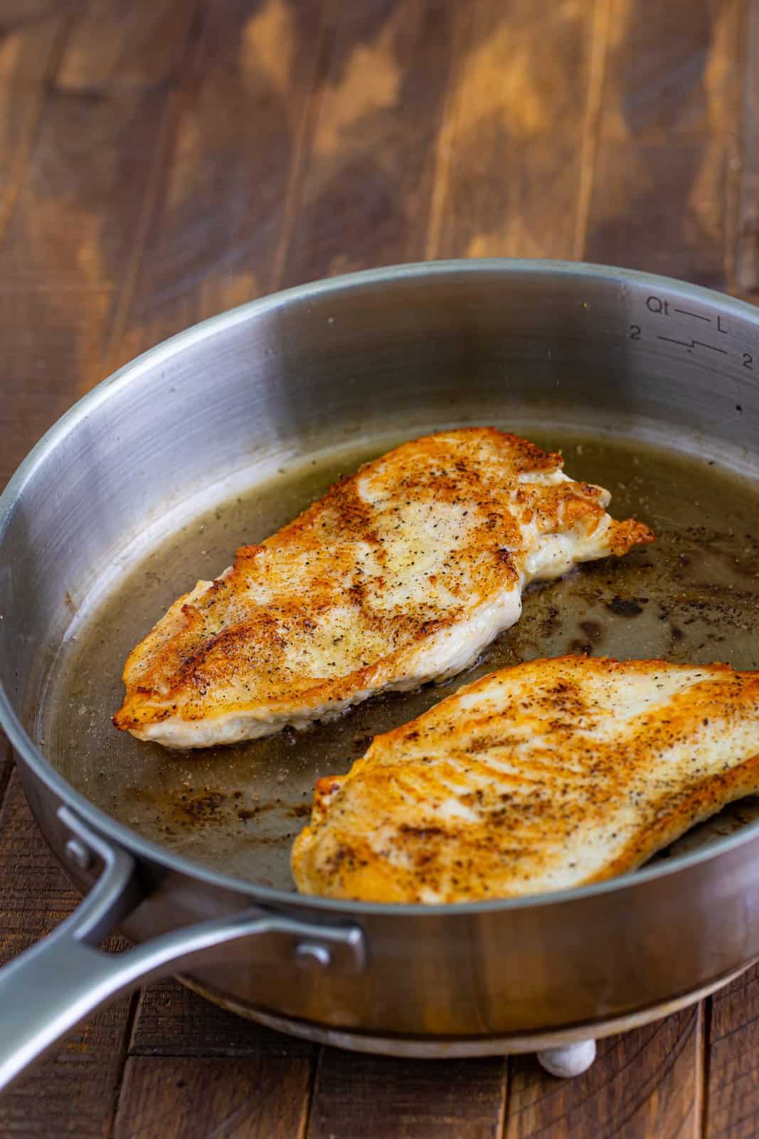 Butterflied chicken breasts in a saucepan with oil.