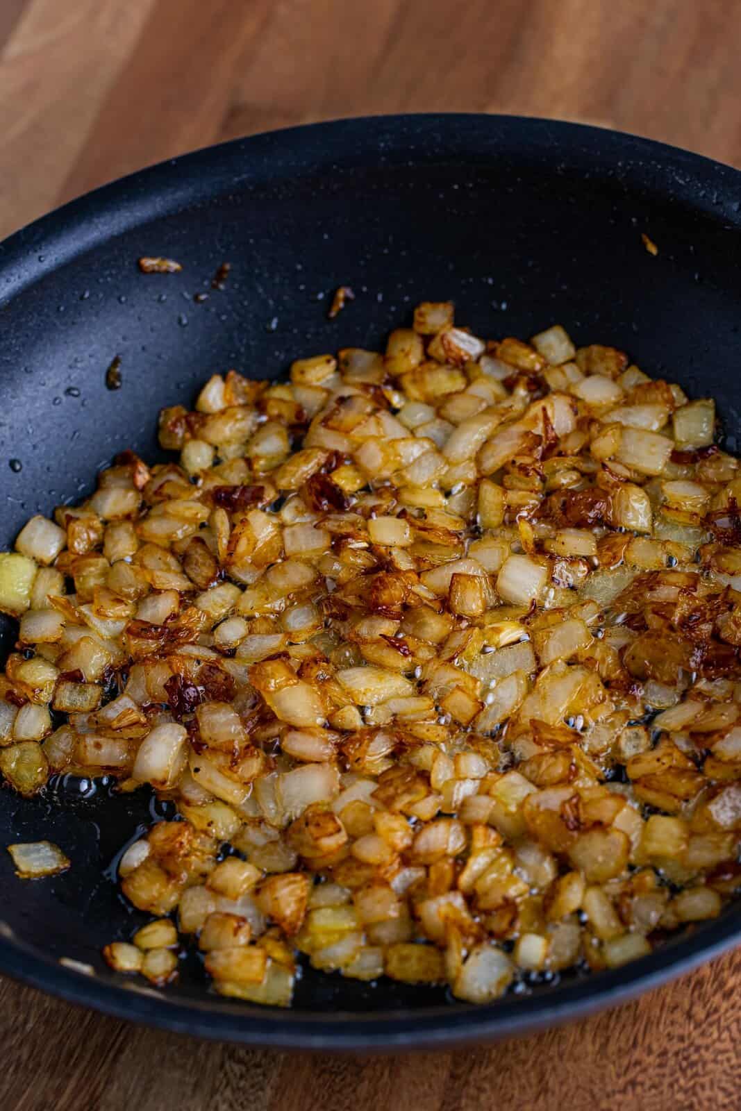 A skillet with cooked onions, pepper, sugar, and butter. 