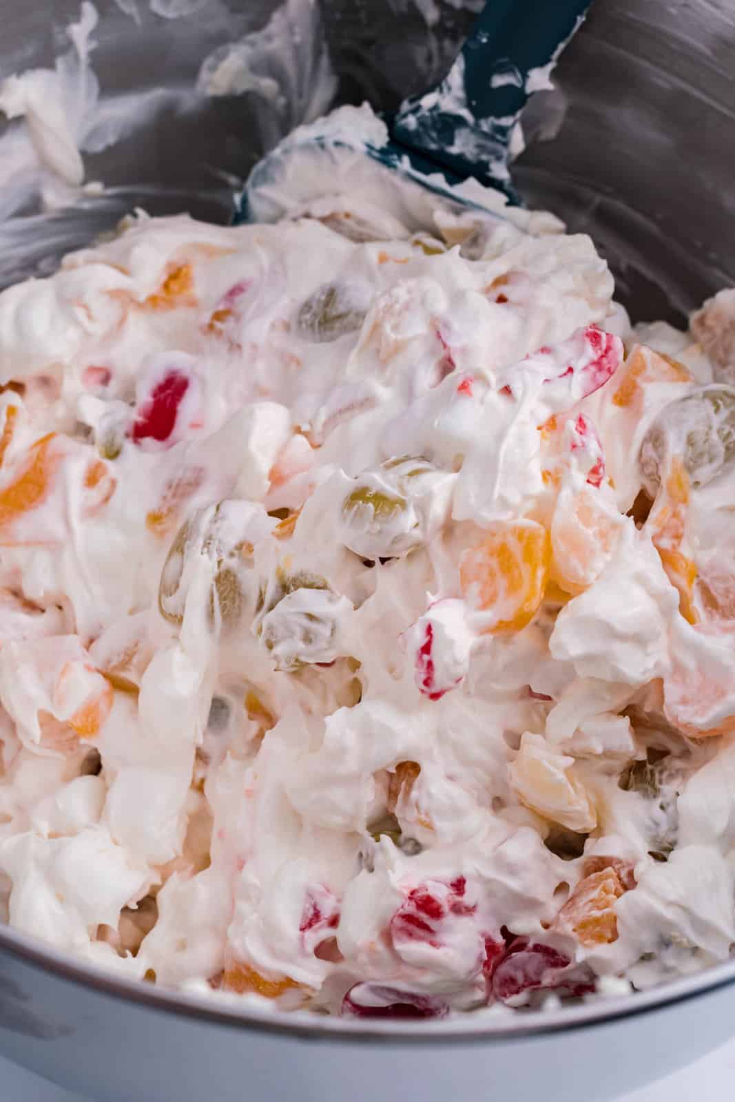A mixing bowl with cream cheese, cool whip, fruit cocktail, marshmallows, and cherries.