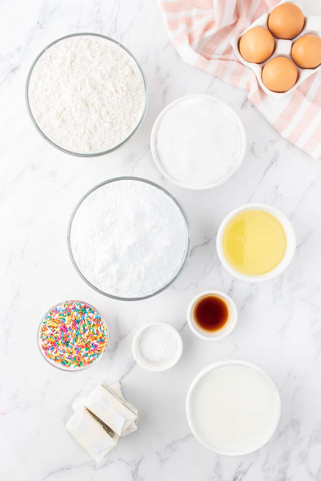 Powdered sugar, vanilla extract, eggs, unsalted butter, all purpose flour, baking powder, salt, vegetable oil, granulated sugar, milk, and rainbow sprinkles.