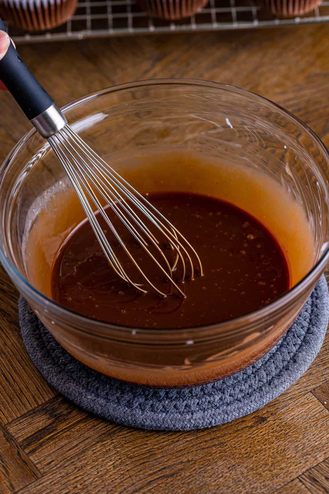 A chocolate ganache in a bowl with a whisk.