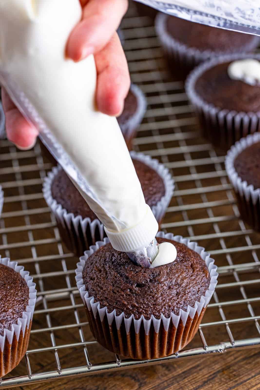 A piping bag full of filling on a chocolate cupcake.