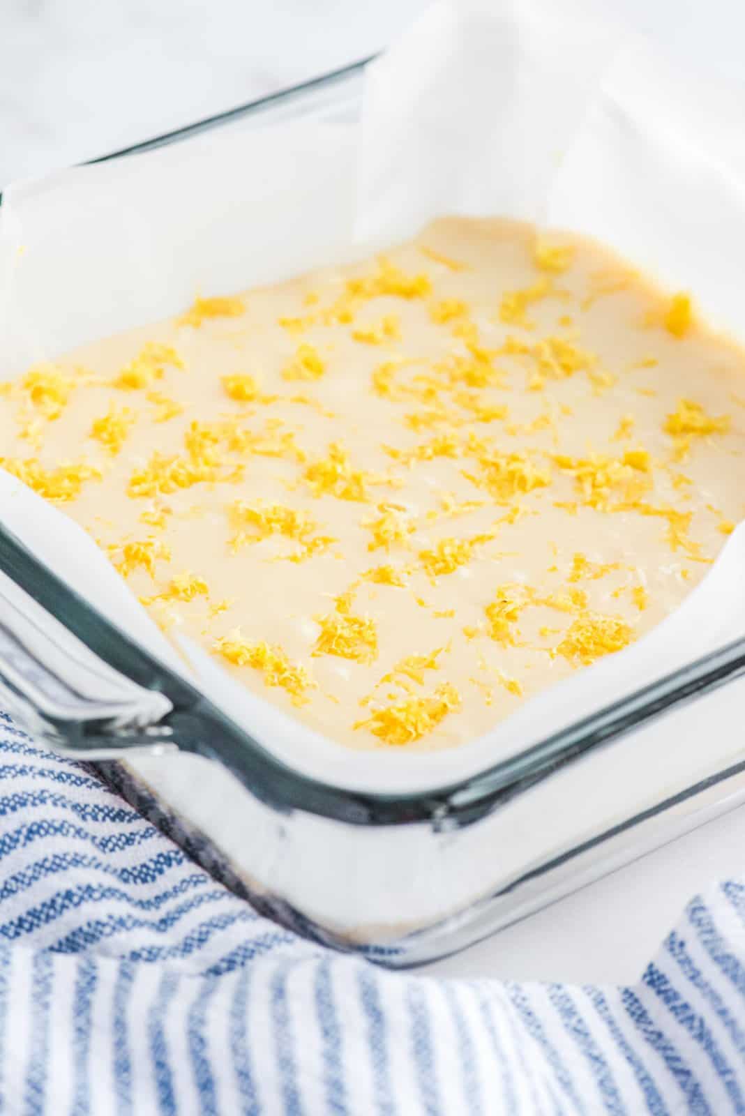 A baking sheet lined with parchment paper with lemon fudge batter with lemon zest on top.