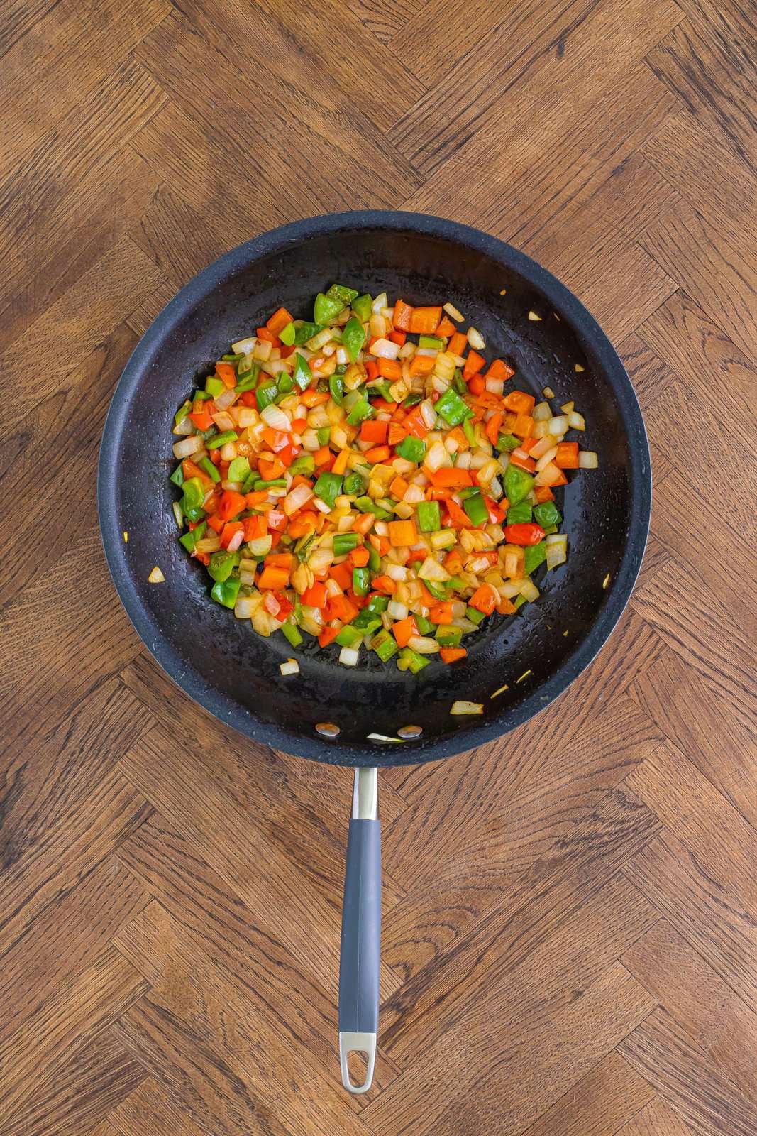A skillet with onion, green bell pepper, and red bell pepper.