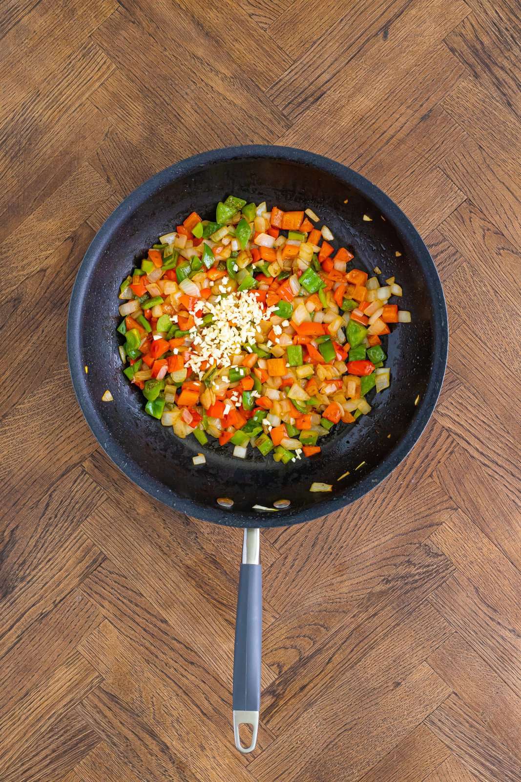 A skillet with onion, green bell pepper, and red bell pepper and garlic. 