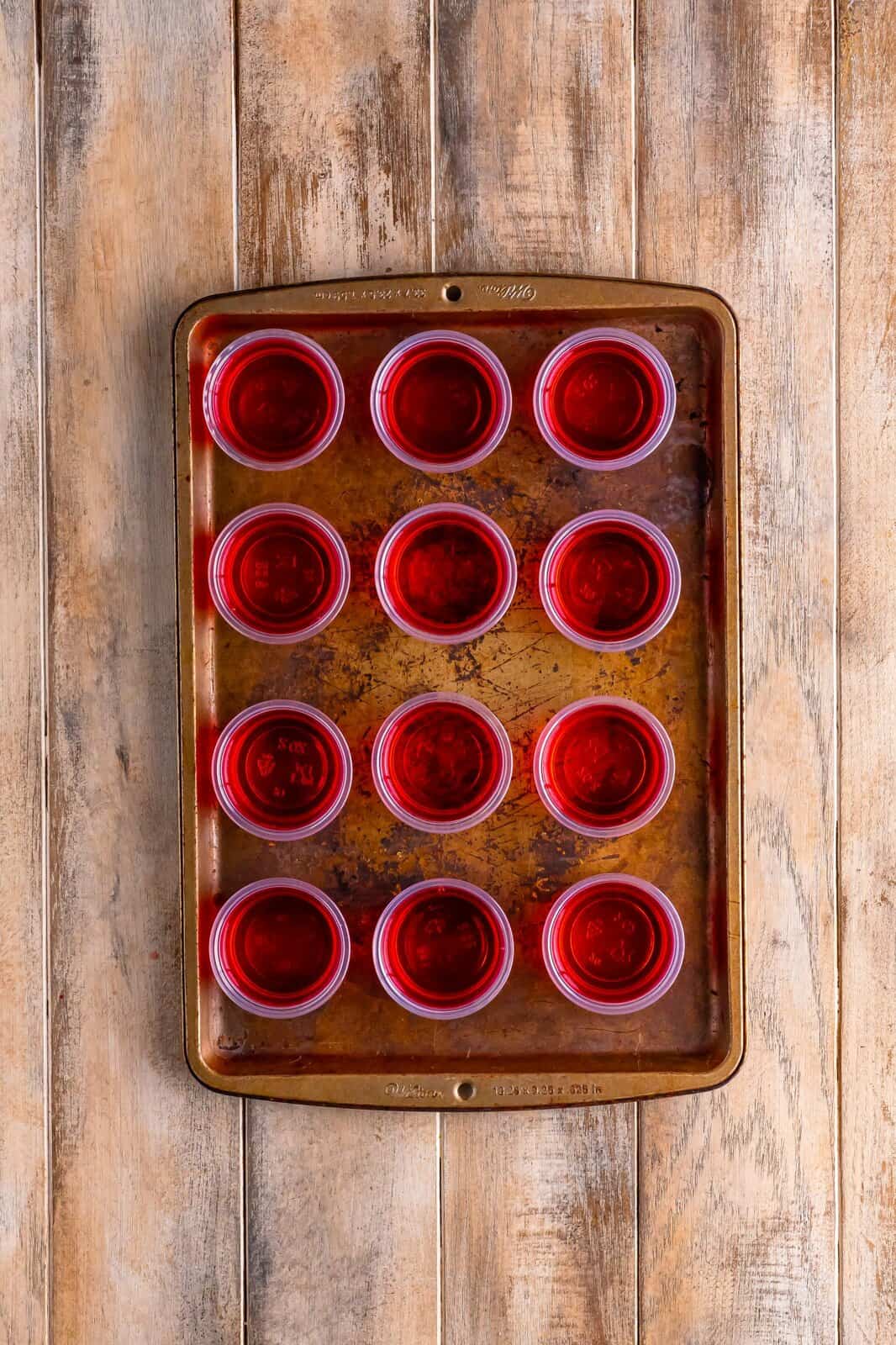 A baking tray of jello shot cups filled up with jello. 
