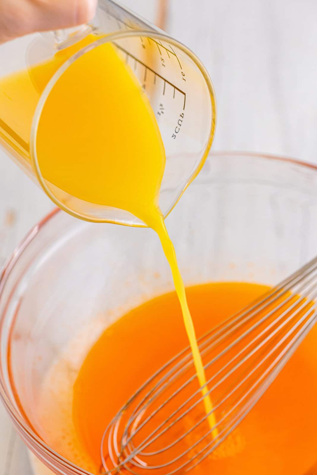 Orange juice being poured in a mixing bowl with orange jello mix, tequila and water. 