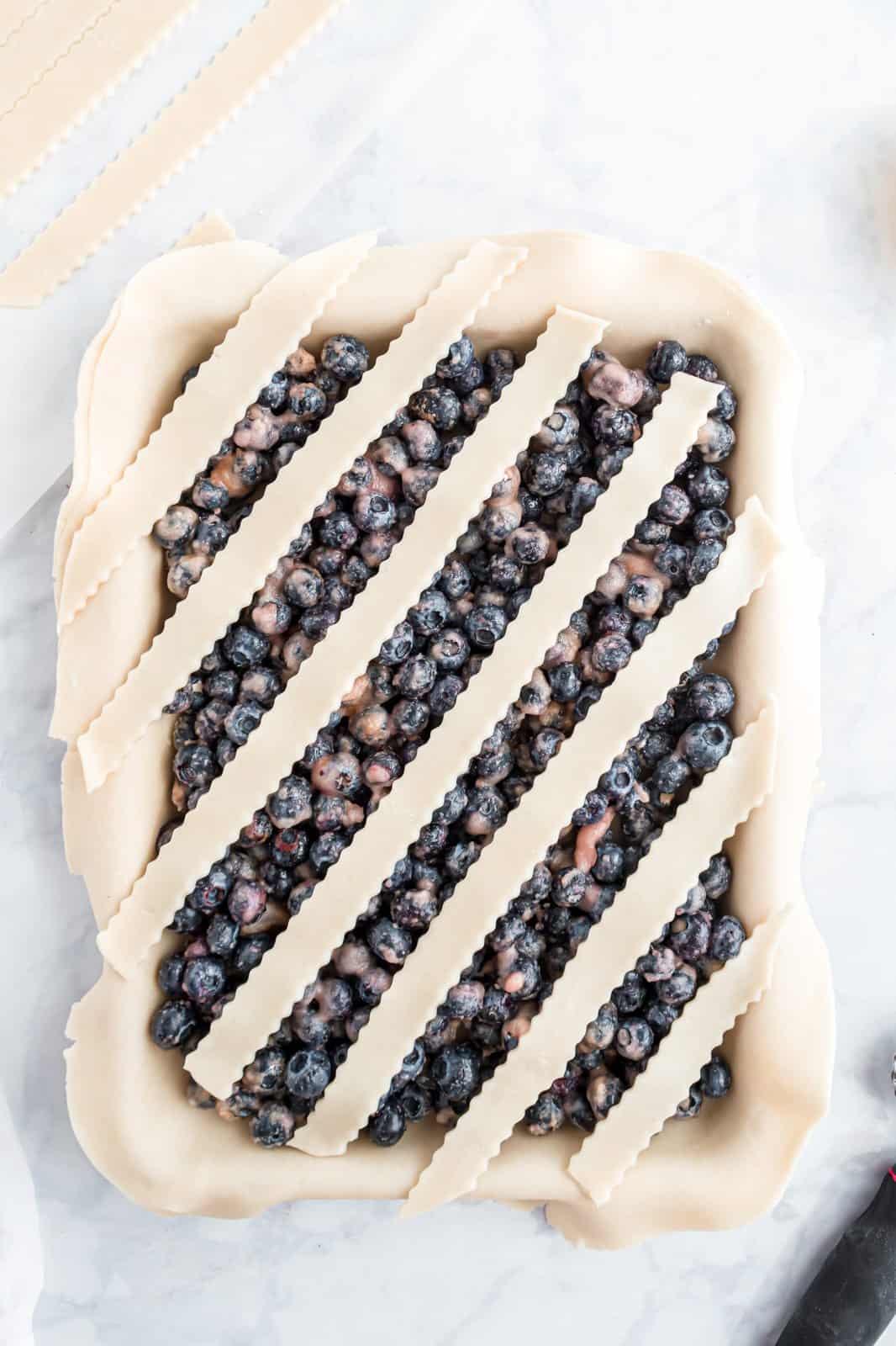 Strips of dough laid out over blueberry pie filing.
