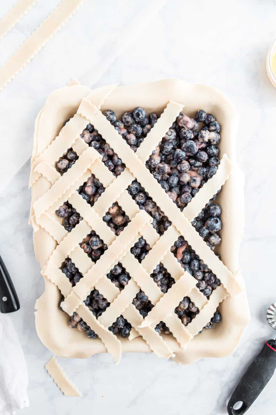 A blueberry slab pie filling with lattice being laid on top.