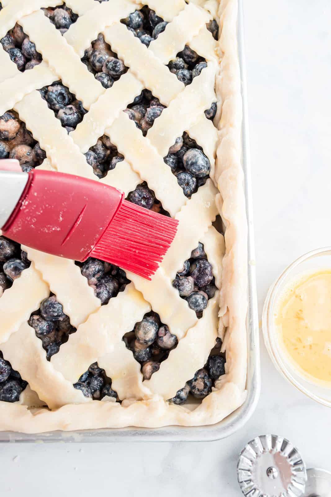A pastry brush adding egg wash on top of the lattice. 