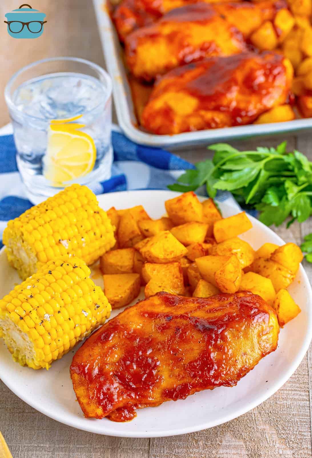 A plate of BBQ Chicken, potatoes, and corn next to a sheet pan.