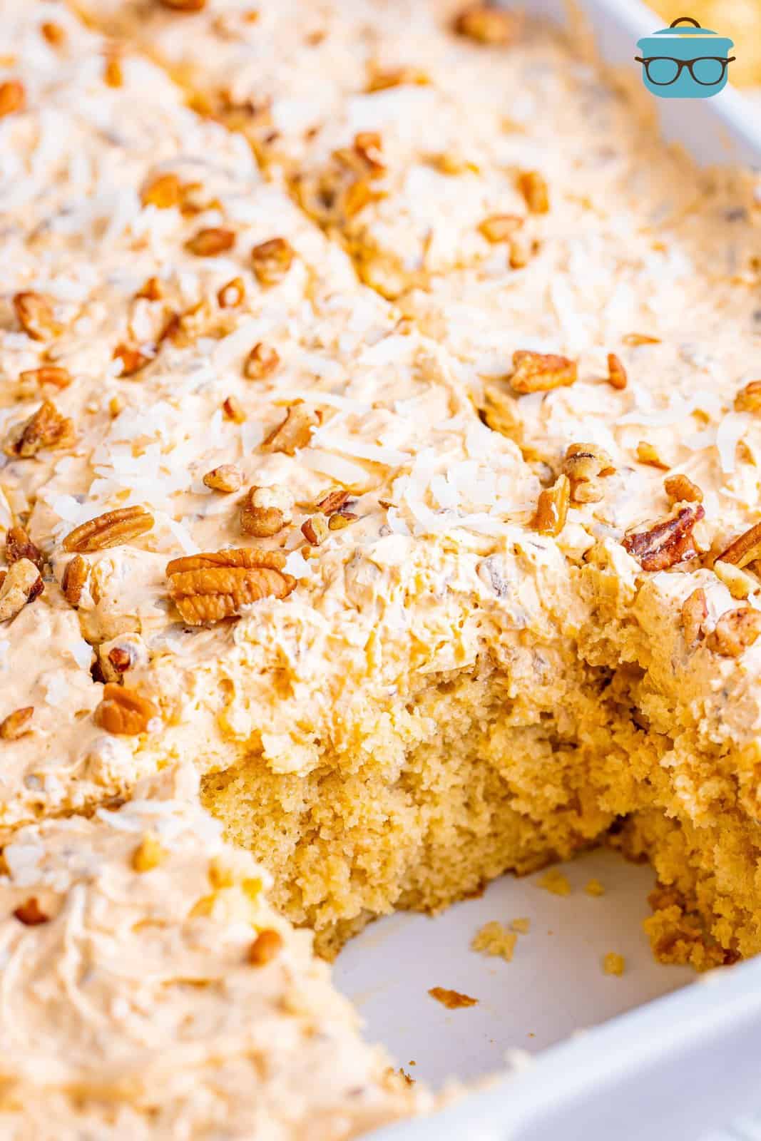 A baking dish of butter pecan poke cake with a piece taken out.