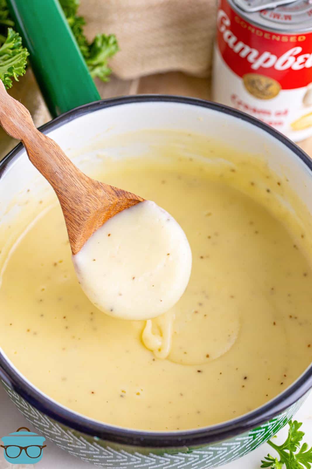 A wooden spoon with some homemade cream of chicken soup on it above the pot of it.