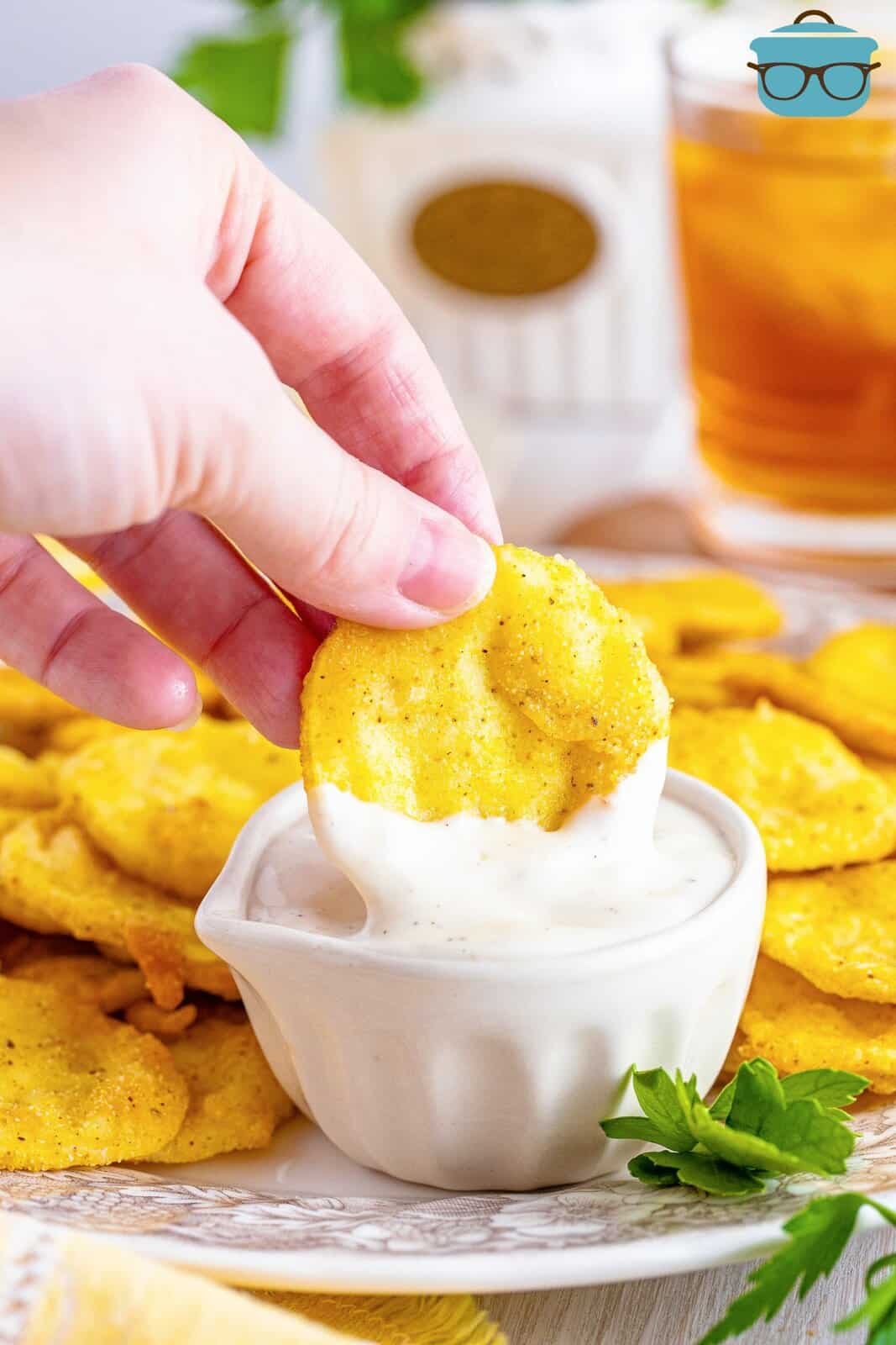 A hand dipping a piece of fried squash in ranch.