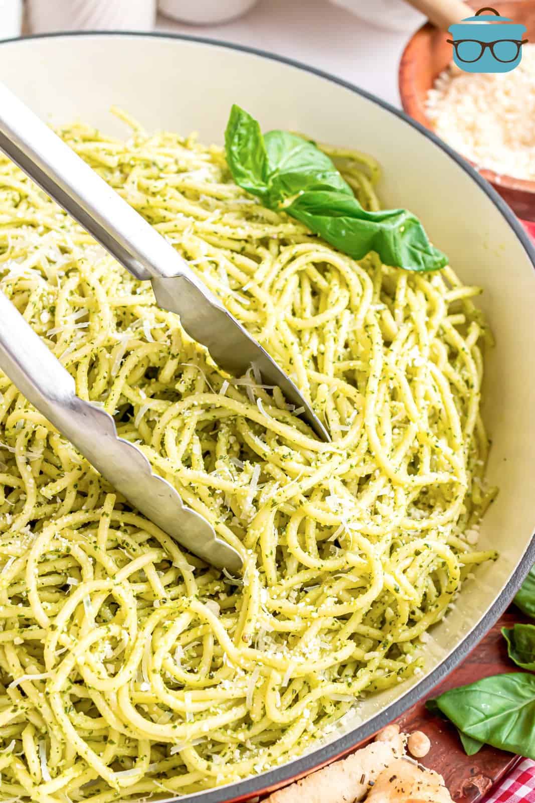 Tongs in a bowl of pasta with pesto sauce.