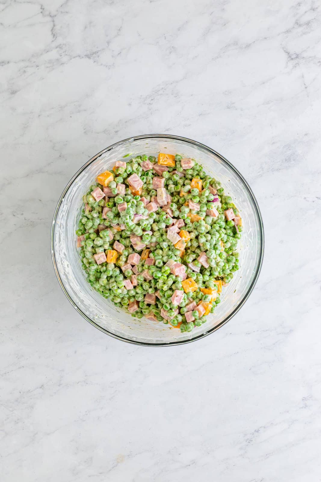 A mixing bowl with the dressing over the peas, ham, cheese, and onion.