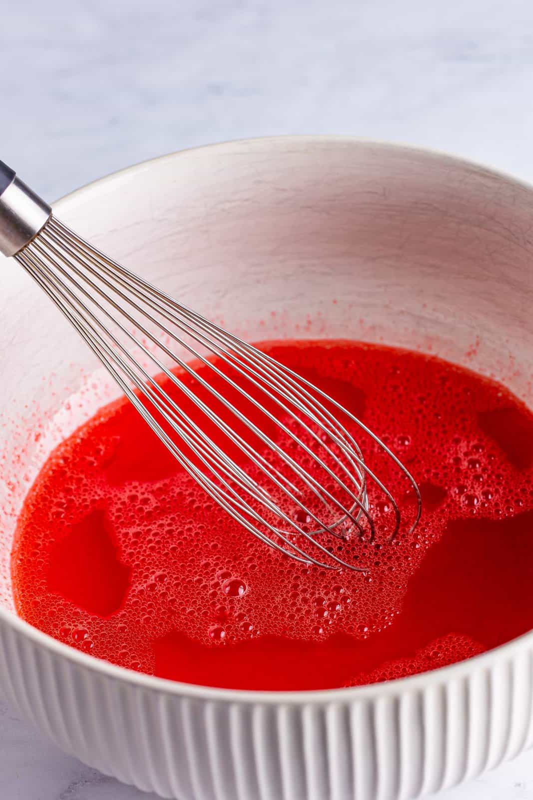 A mixing bowl with strawberry banana jello and water. 
