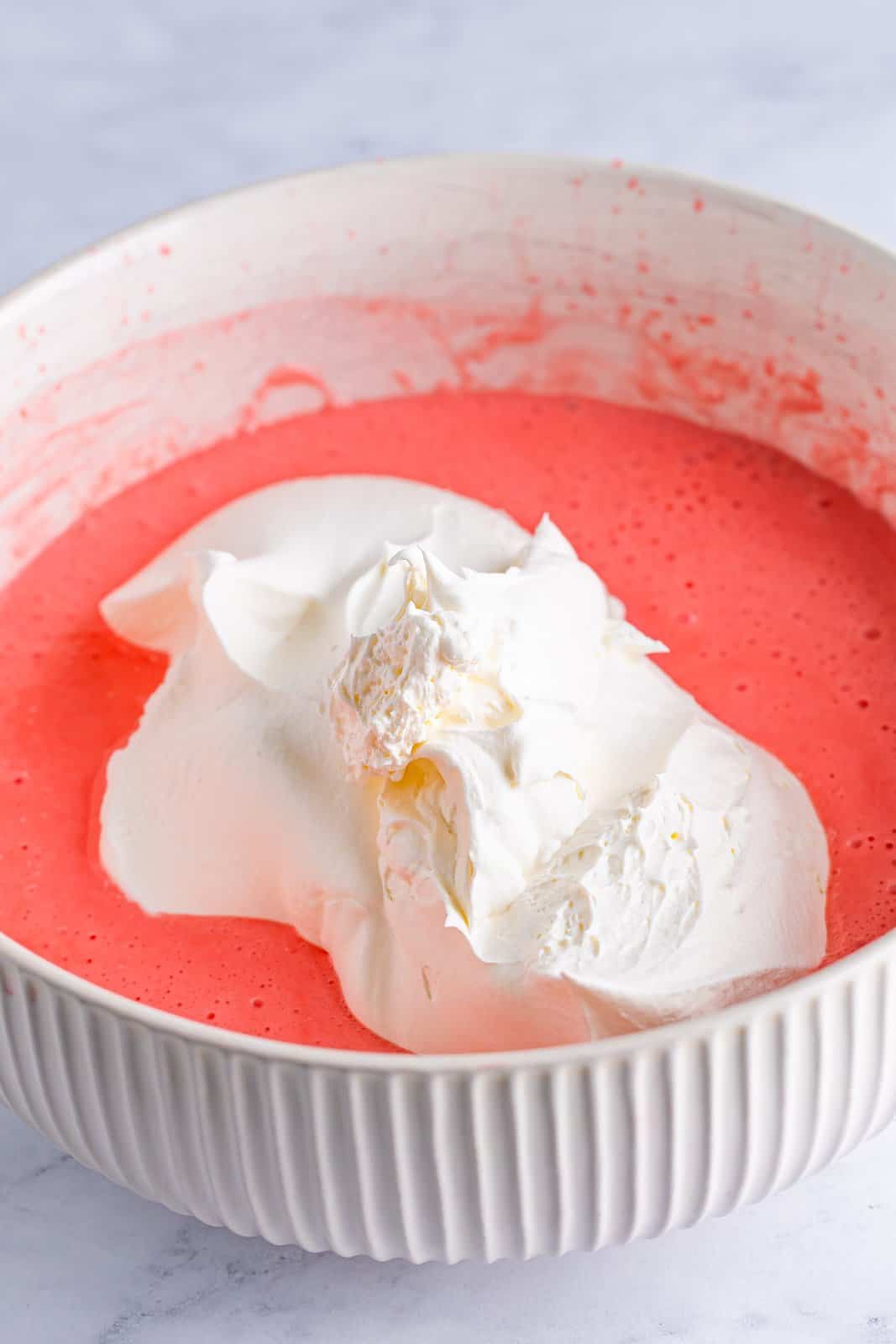 A mixing bowl with strawberry banana jello, whipped topping, and cream cheese. 