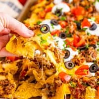 Close up looking at nachos and a hand holding a loaded nacho chip.