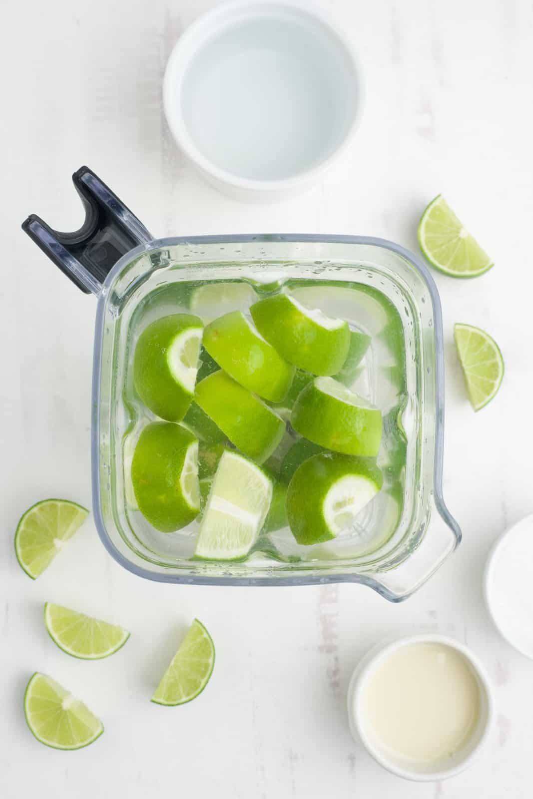 A blender with lime wedges, sugar and water.