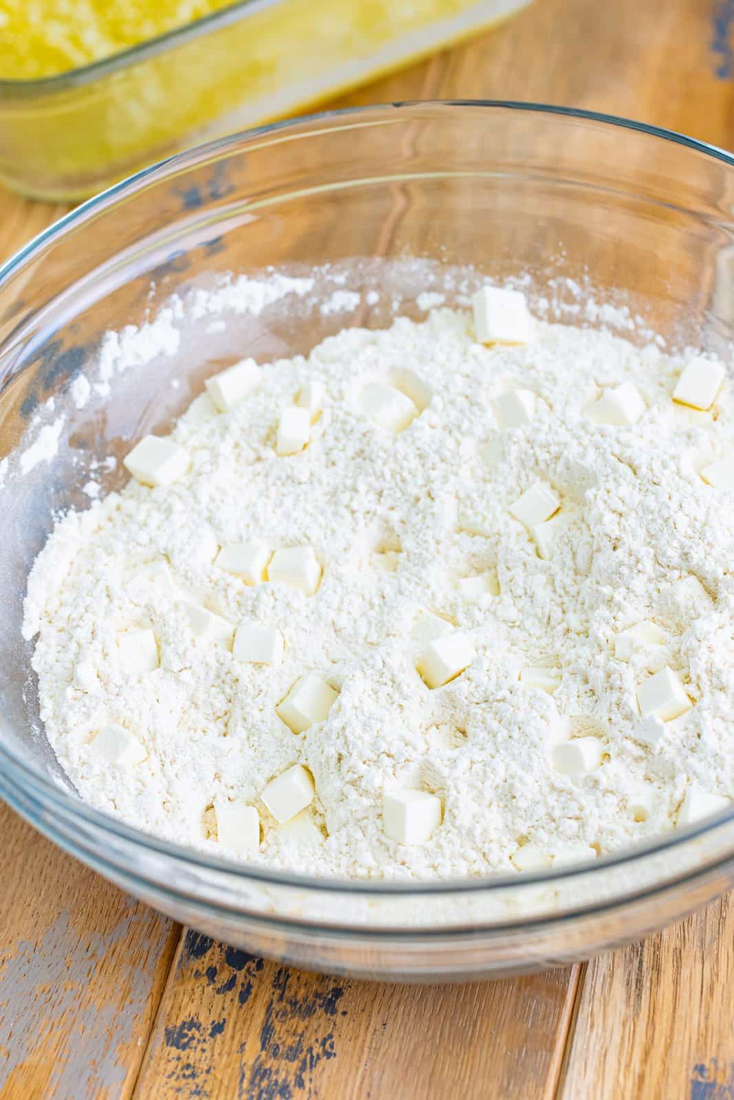 A mixing bowl with  flour, sugar, baking powder, salt, cream cheese cubes, garlic powder, and onion powder.