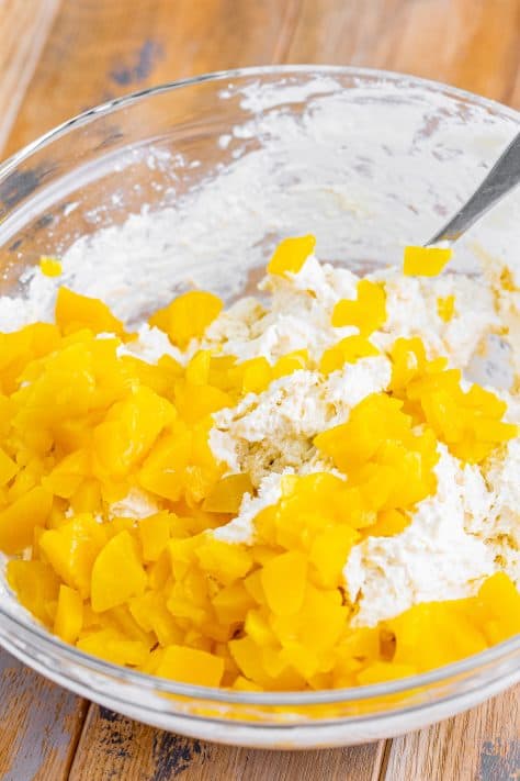A mixing bowl with flour, sugar , heavy cream, vanilla, peach chunks, and baking powder.