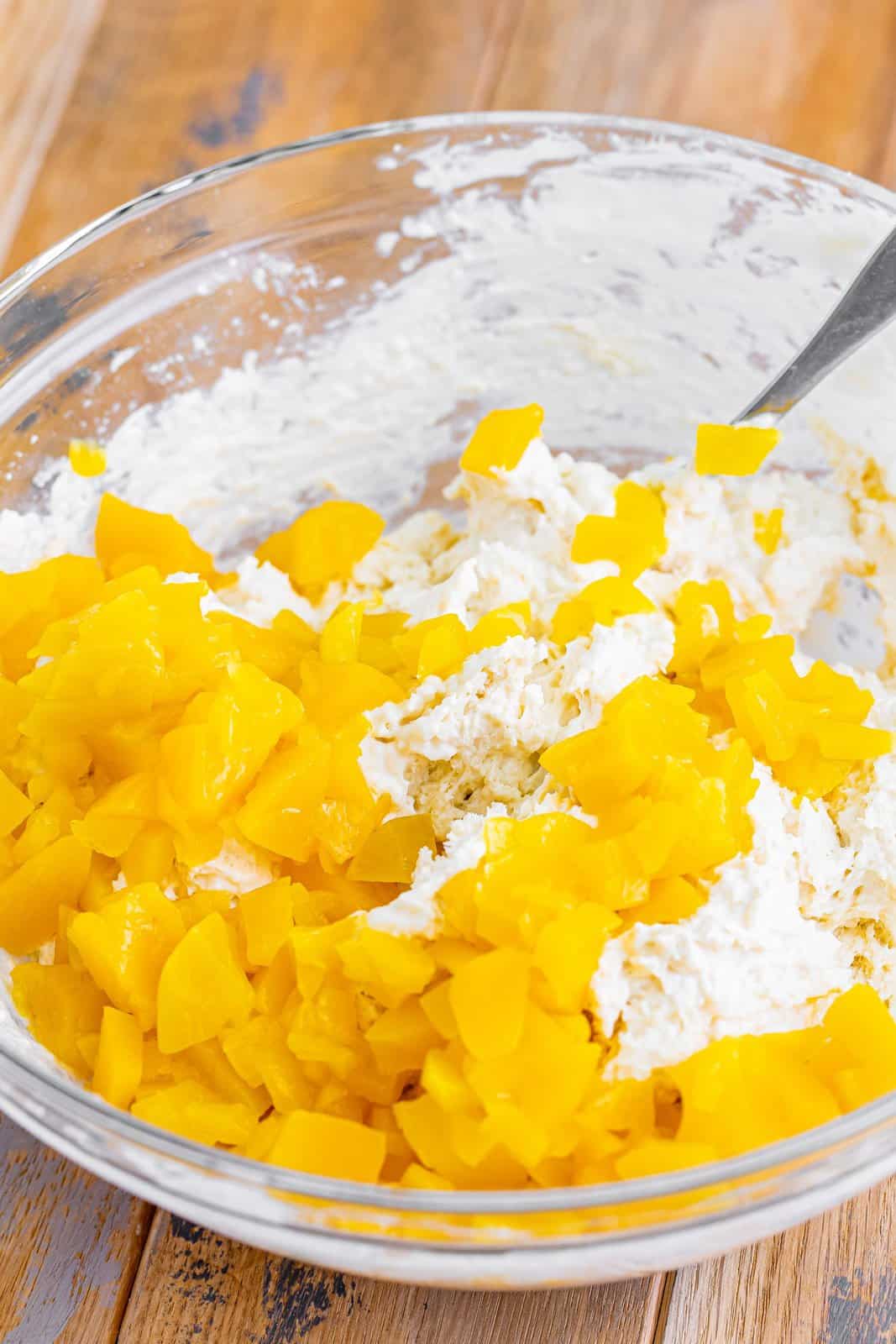 A mixing bowl with flour, sugar , heavy cream, vanilla, peach chunks, and baking powder. 