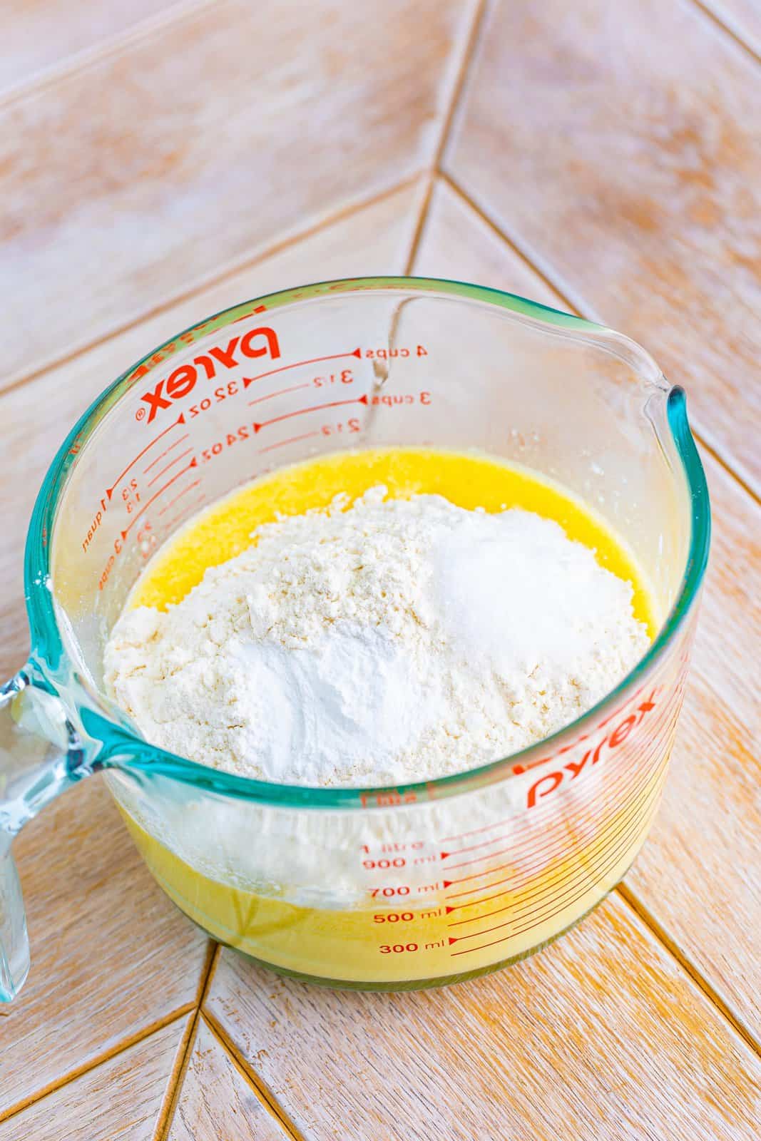 A measuring cup used as a bowl with milk, butter, oil, eggs, flour, baking soda, and salt. 
