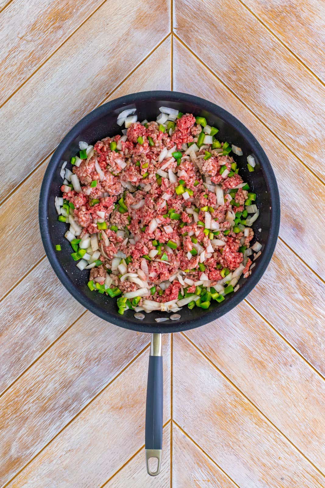 A skillet with ground beef and Italian sausage along with the onion and green pepper.
