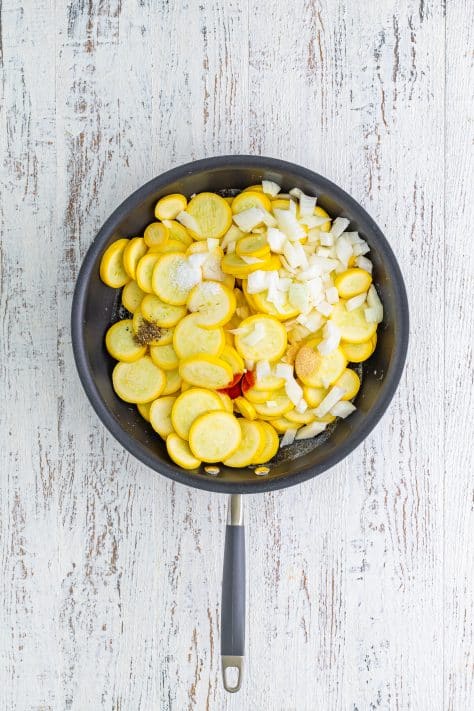 A skillet with melted butter, squash, onion, salt, pepper, garlic powder, and paprika.