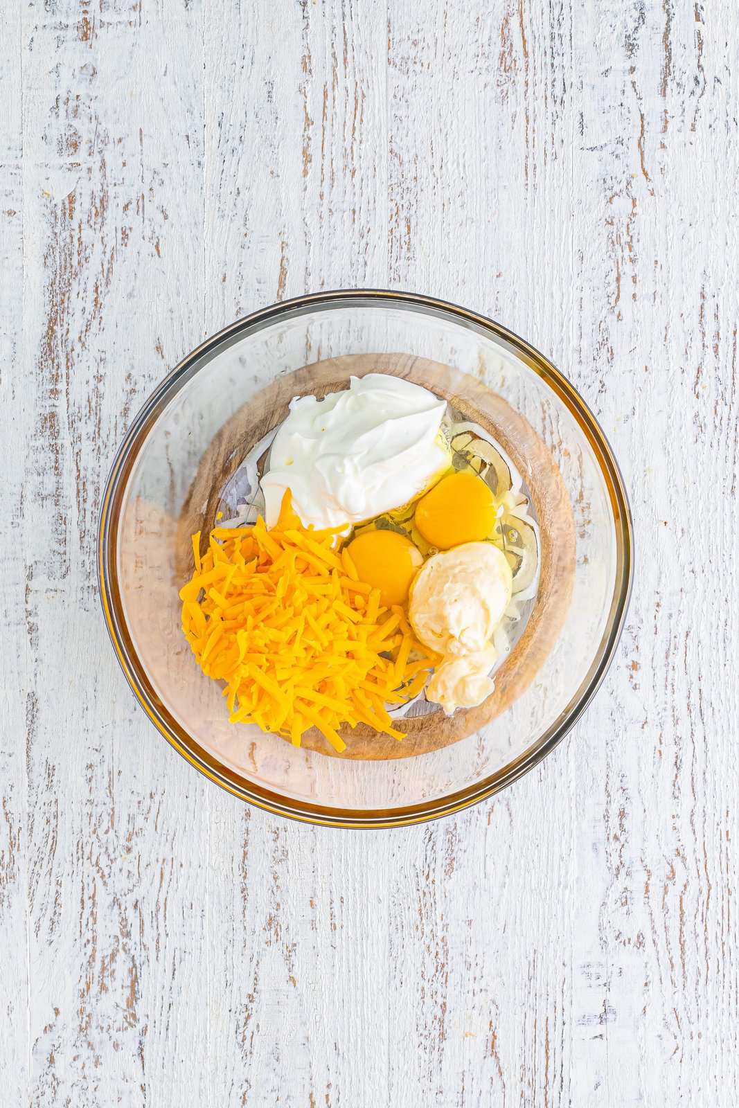 A mixing bowl with eggs, sour cream, mayonnaise, and cheese.