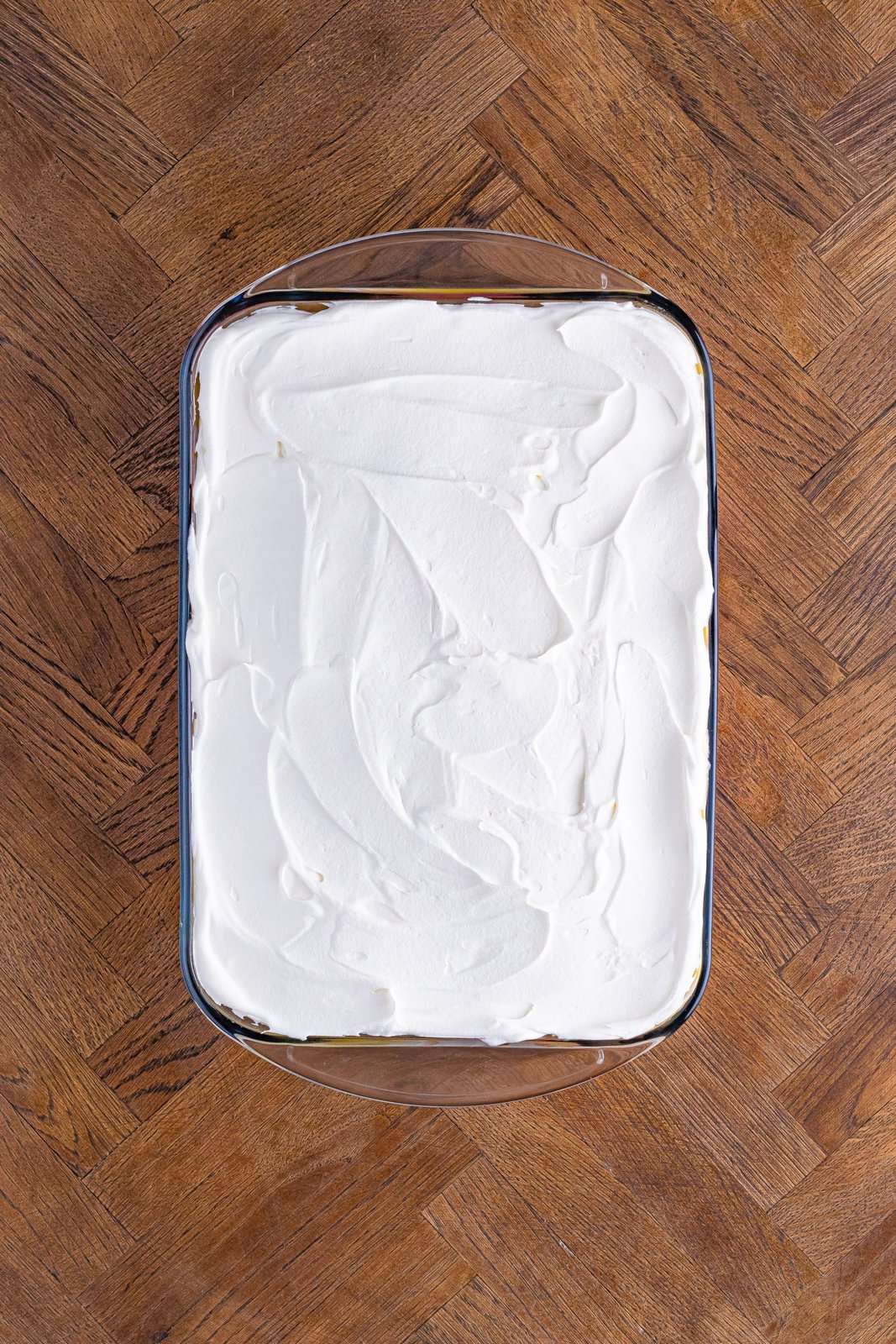 A Cool Whip layer smoothed out over top of the dessert in a baking dish.