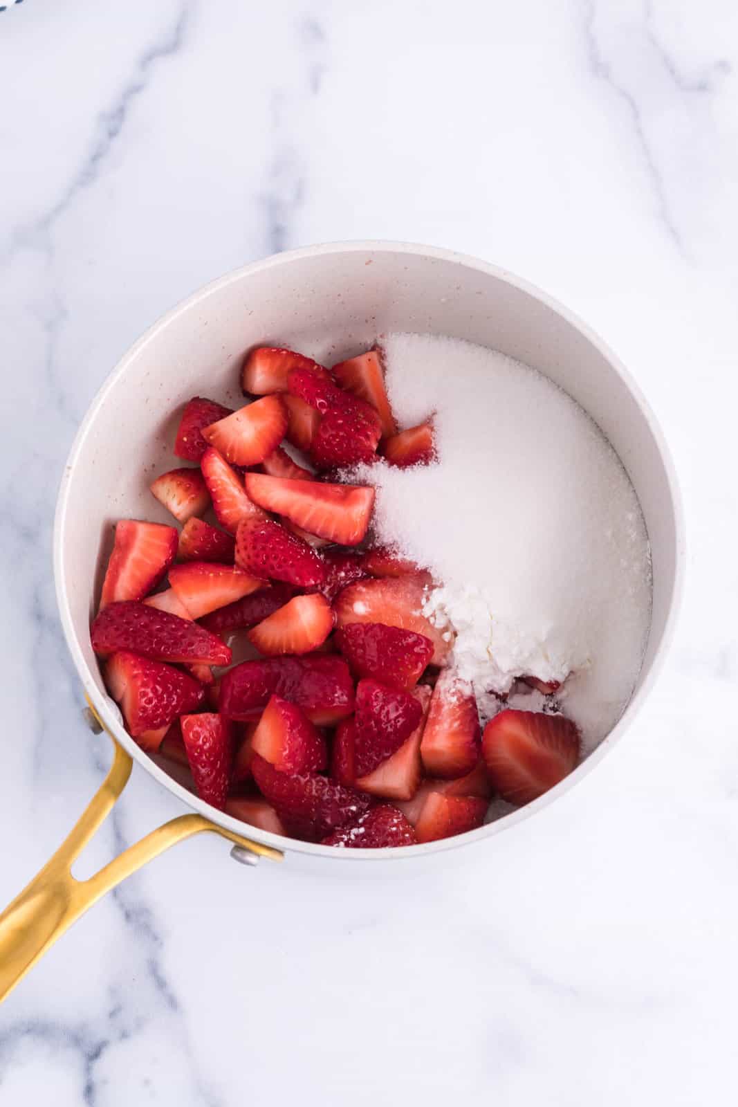 A saucepan with strawberries and sugar. 