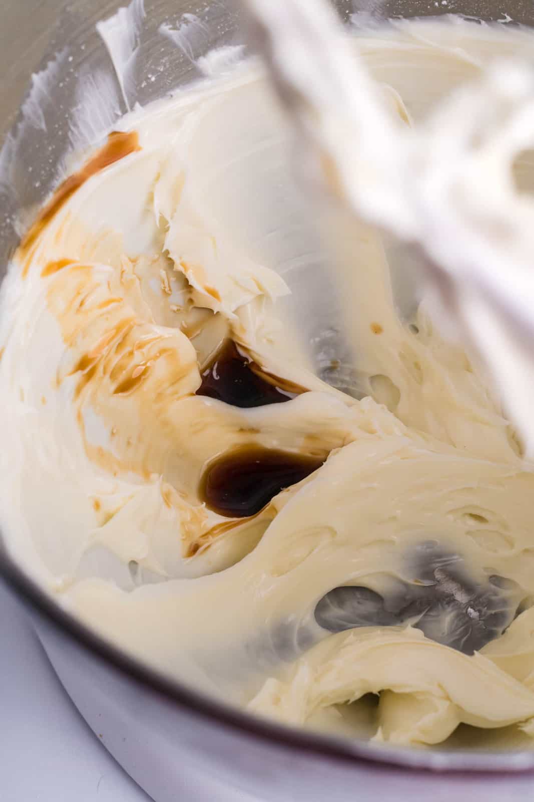 A cream cheese, vanilla extract, and powdered sugar  being mixed in a bowl.
