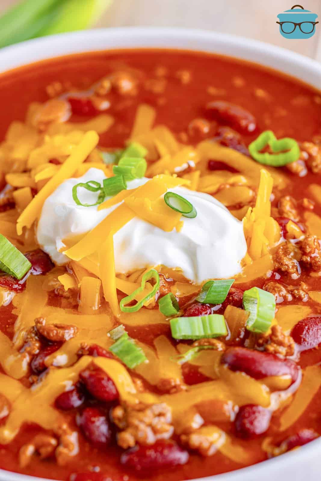 Close up looking at a bowl of chili with shredded cheese, sour cream and chives on top.