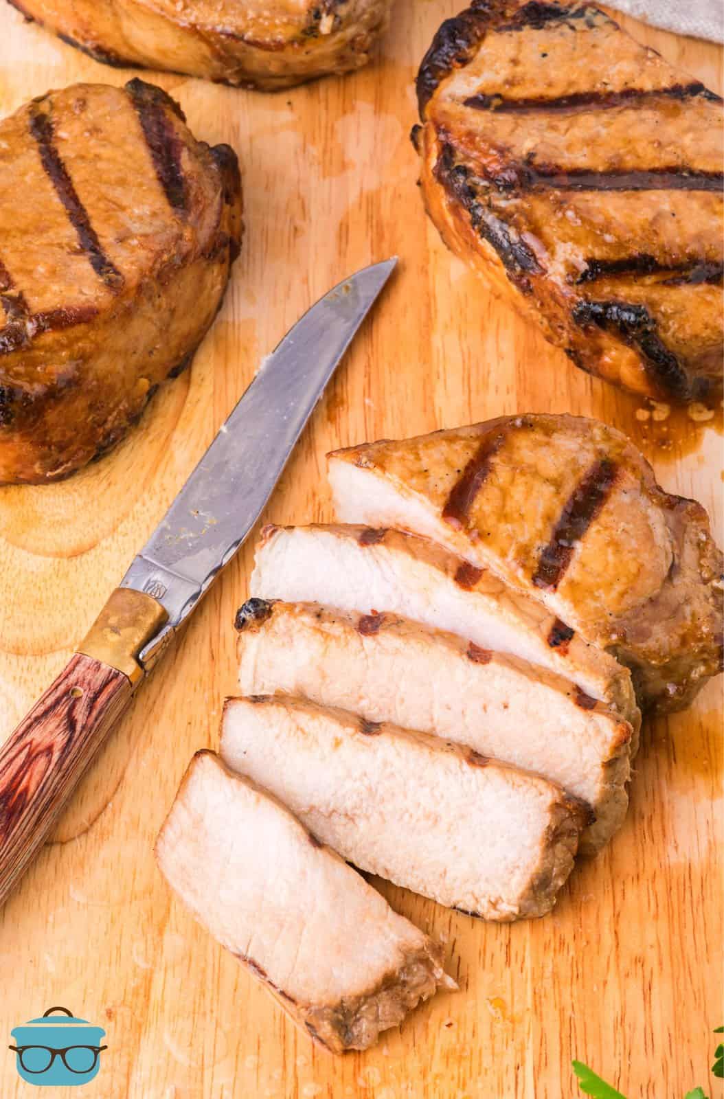 A cutting board with a knife next to a cut up Grilled Pork Chop.