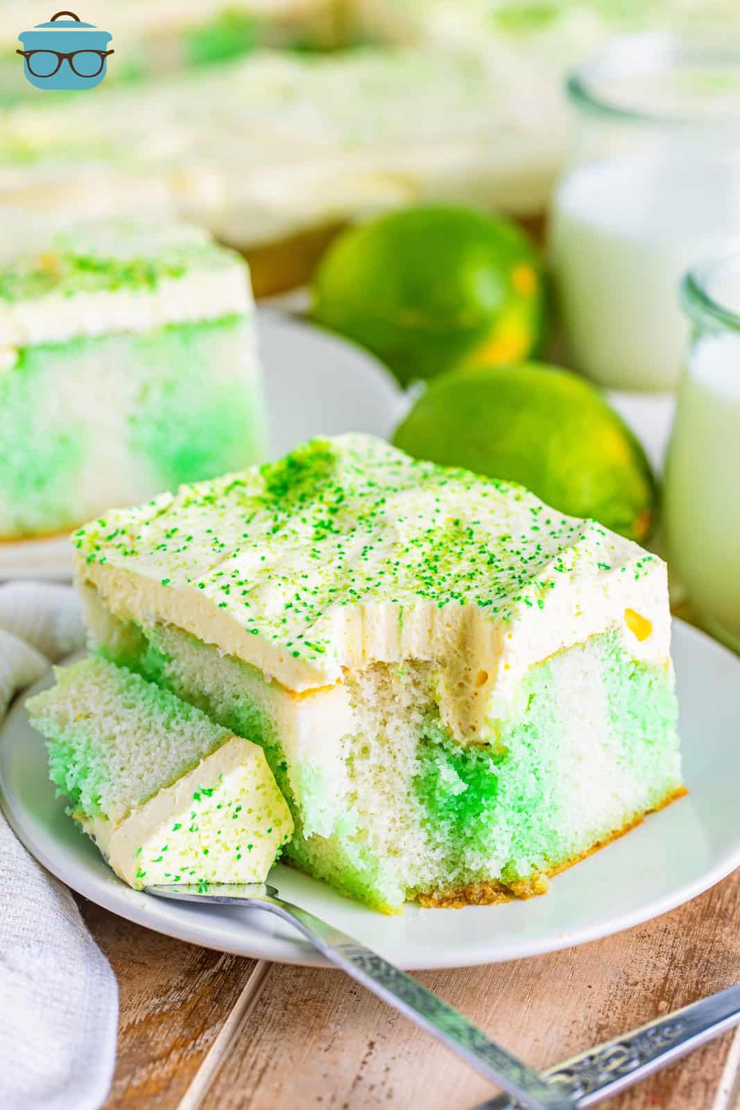 A slice of Lime Jello Poke Cake on a plate with a bite taken out.