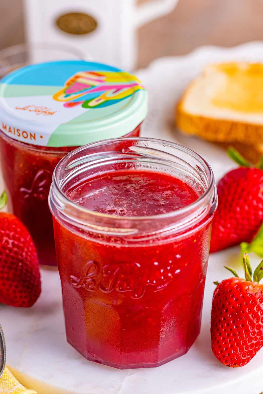 An open and closed jar of Strawberry Jam. 