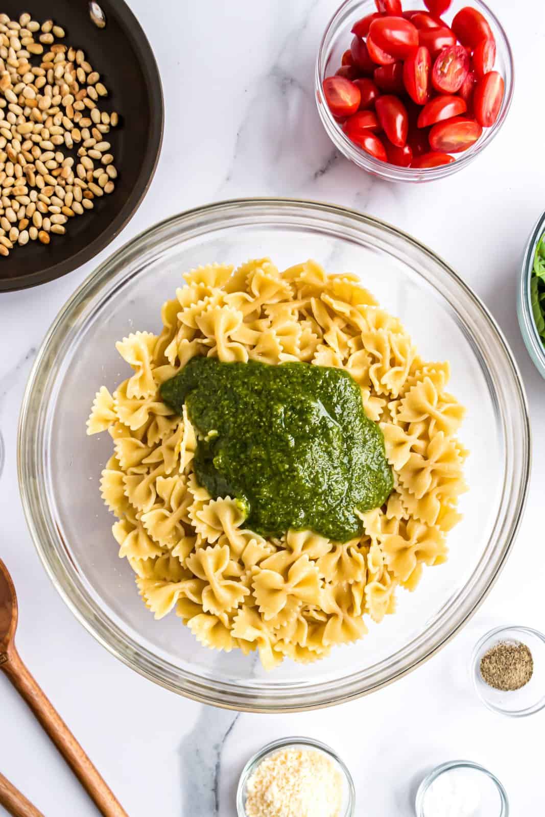 Pesto and lemon juice sitting in a bowl of cooled farfalle pasta. 