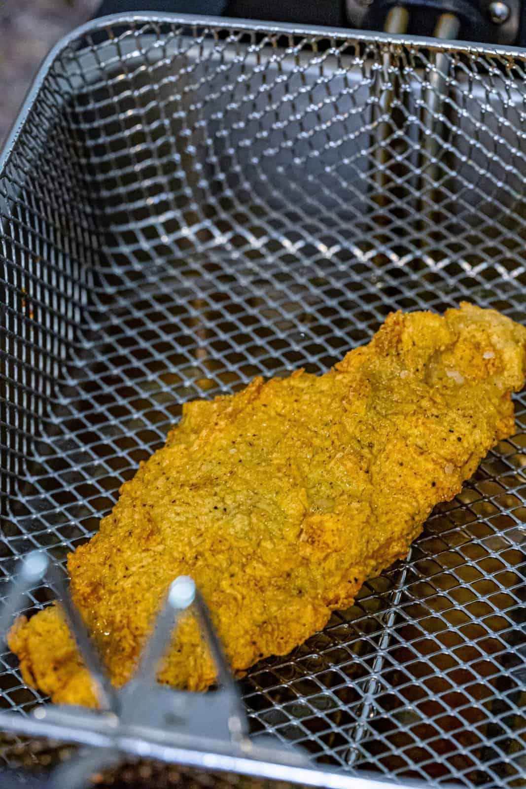 A fried catfish filet in a fryer basket. 