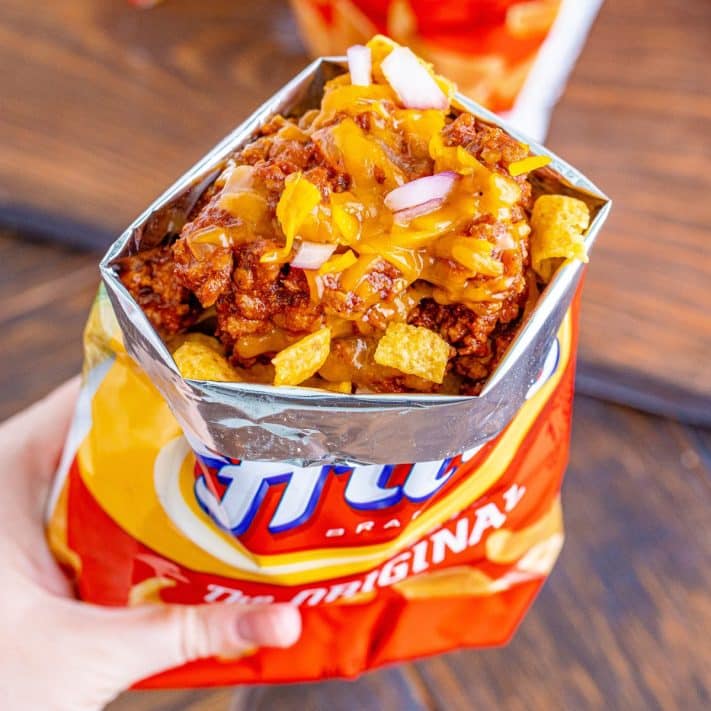 a bag of Fritos cut open with chili, cheese and diced onions on top.