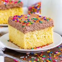 Close up looking at a slice of yellow cake with chocolate frosting and sprinkles.